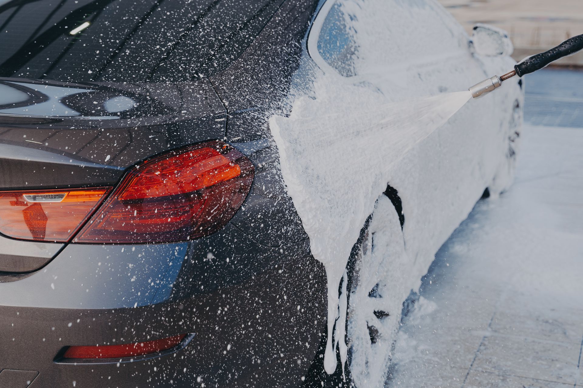 A dark car being sprayed with white foam, likely for washing.