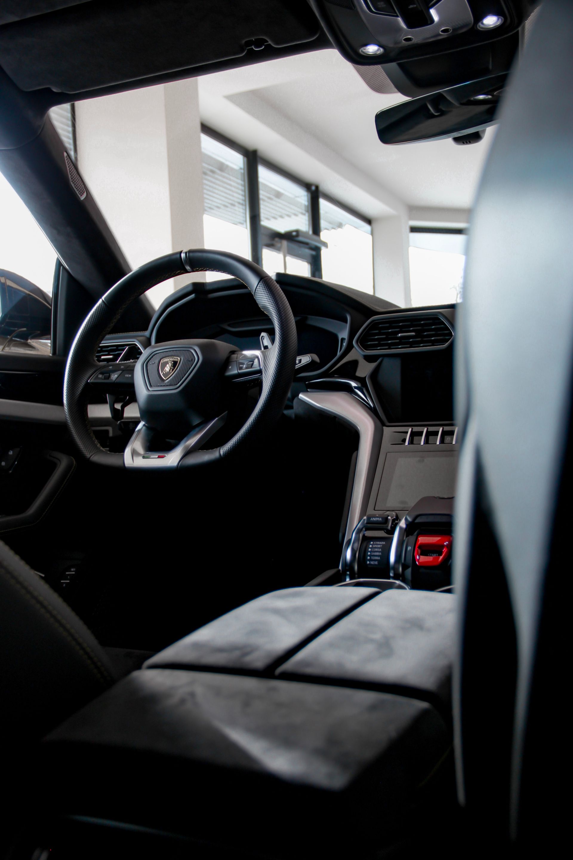 Interior view of a black Lamborghini Urus SUV, featuring the steering wheel, console, and part of the seat.