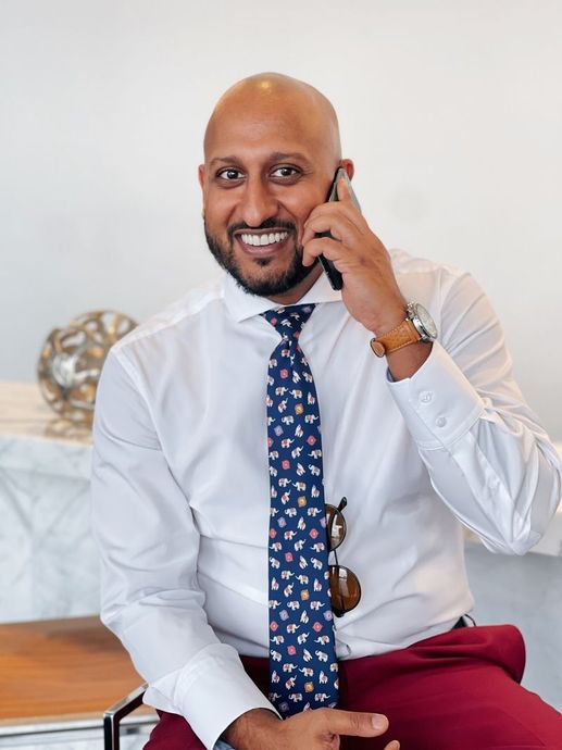 Man in white shirt and patterned tie on the phone, smiling. Wearing red pants, indoors, neutral background.