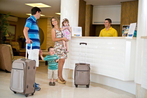Uma família está parada em frente ao balcão de um hotel com bagagens.