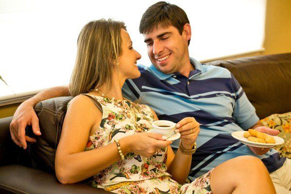 Um homem e uma mulher estão sentados em um sofá tomando café e comendo biscoitos
