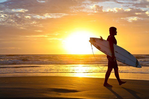 Um homem está carregando uma prancha de surf na praia ao pôr do sol.