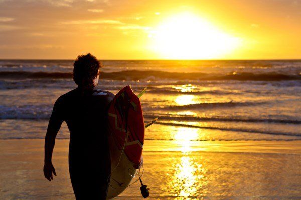 Um homem está carregando uma prancha de surf na praia ao pôr do sol.