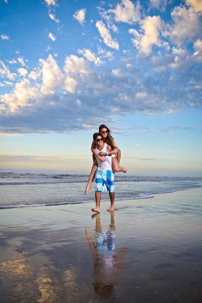 Um homem carrega uma mulher nos ombros na praia.