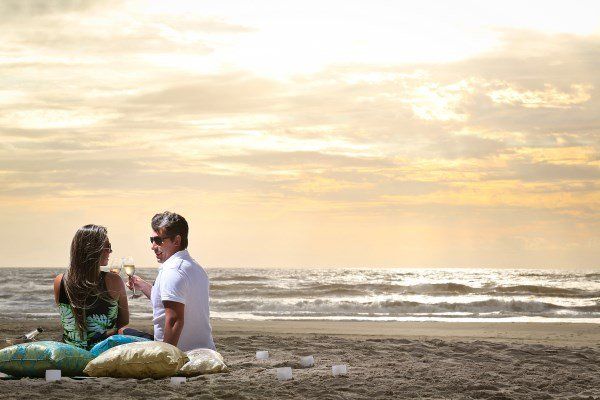 Um homem e uma mulher estão sentados na praia bebendo vinho.