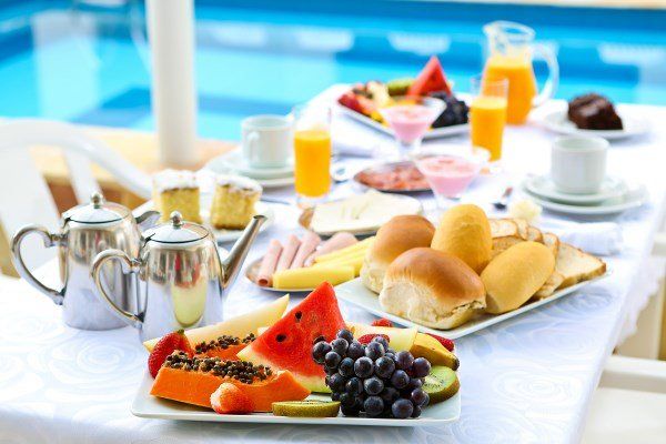 Uma mesa com pratos de comida e bebidas ao lado de uma piscina.