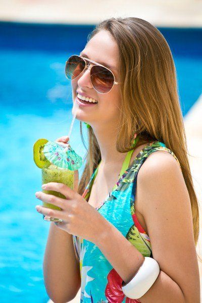 Uma mulher está bebendo um canudo à beira de uma piscina.