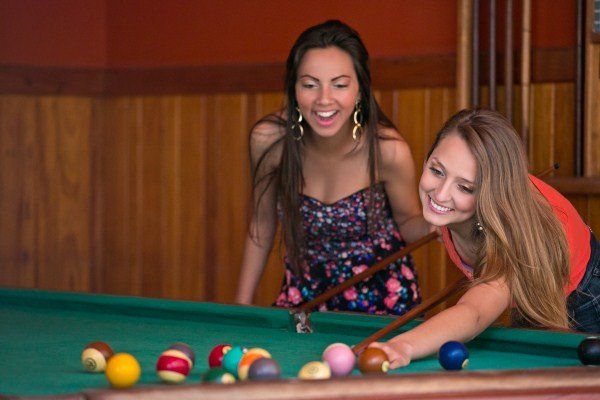 Duas mulheres estão jogando sinuca juntas em um salão de sinuca.