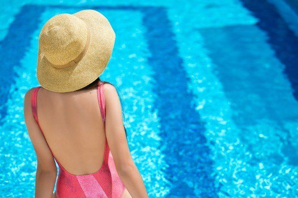 Uma mulher de maiô rosa e chapéu está ao lado de uma piscina.