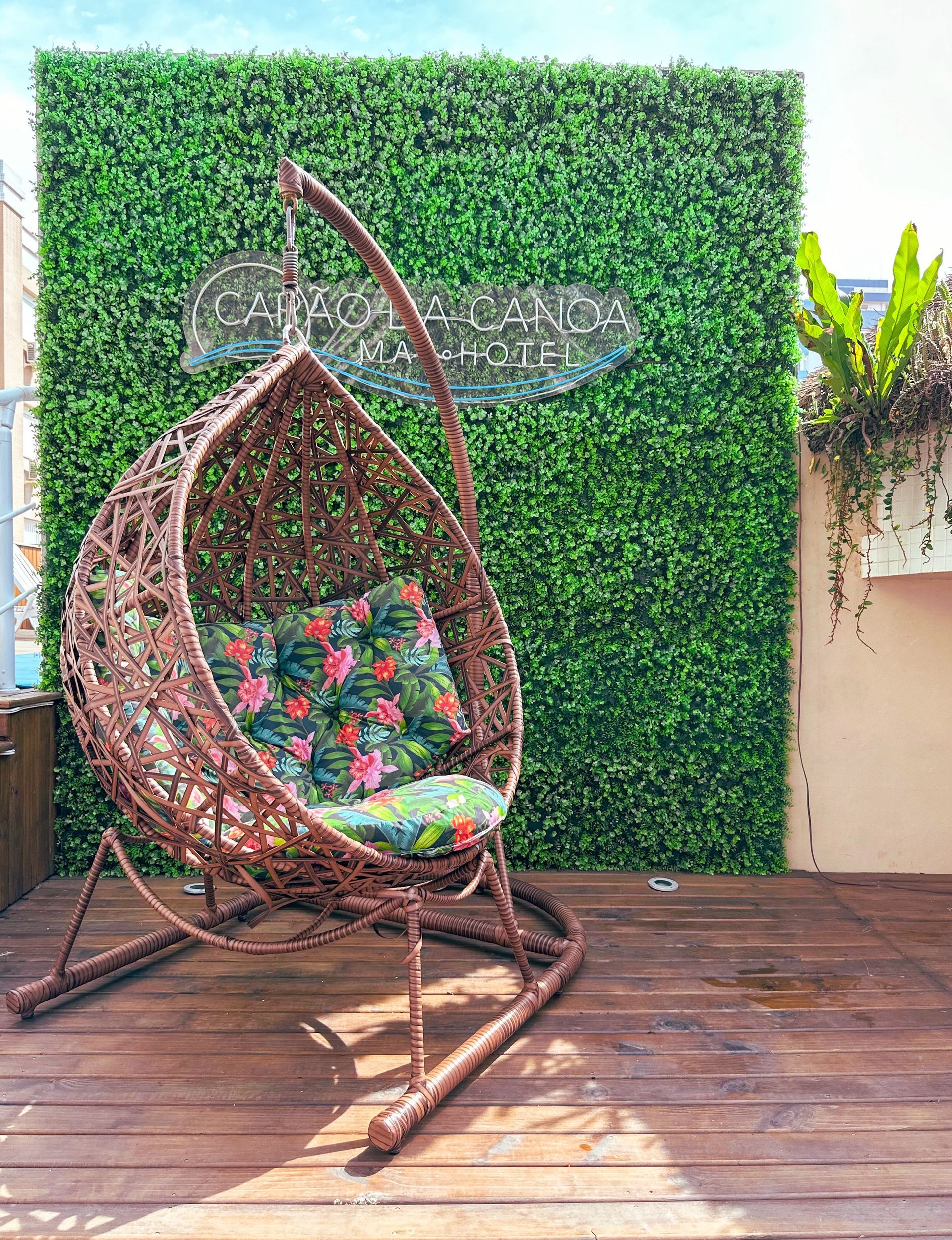 Uma cadeira suspensa de vime está sentada em um deck de madeira em frente a uma parede verde.