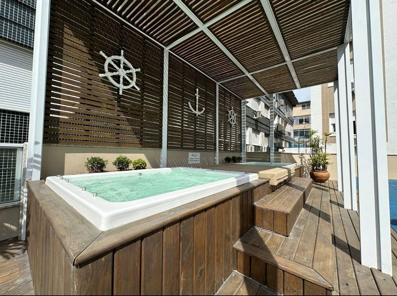 Uma banheira de hidromassagem está sob uma pérgula em um deck de madeira.