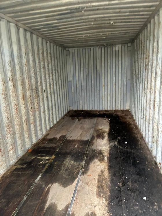 Interior of a shipping container, empty. Metal walls, floor has dark stains and water marks.