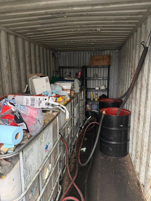 Inside a shipping container: liquid storage tanks, a barrel, shelves with supplies, and hoses.