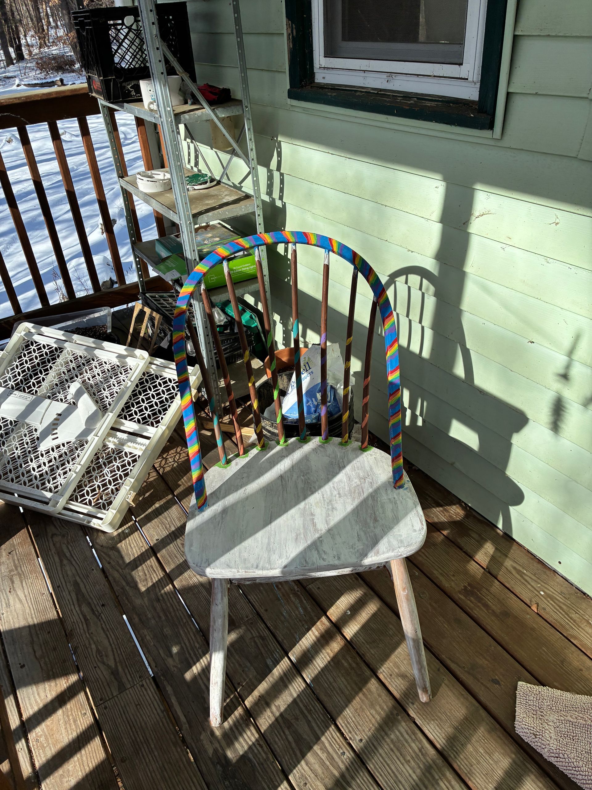 Wooden chair with painted blue and yellow accents on a wooden porch, sunlight.