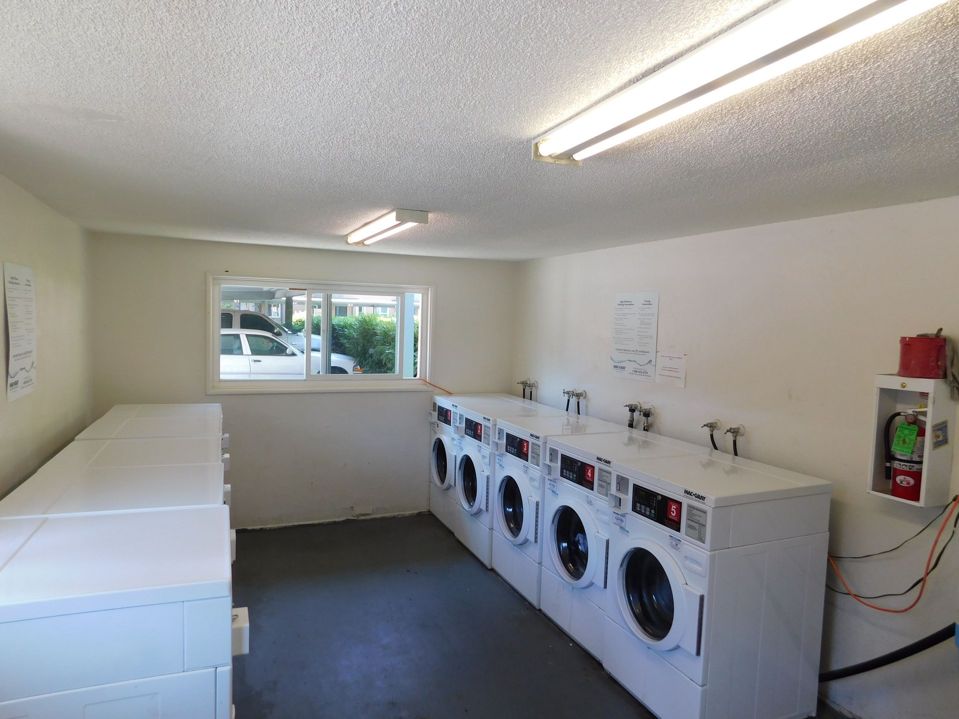 Laundry room with white washers and dryers, a long folding table, and a window.