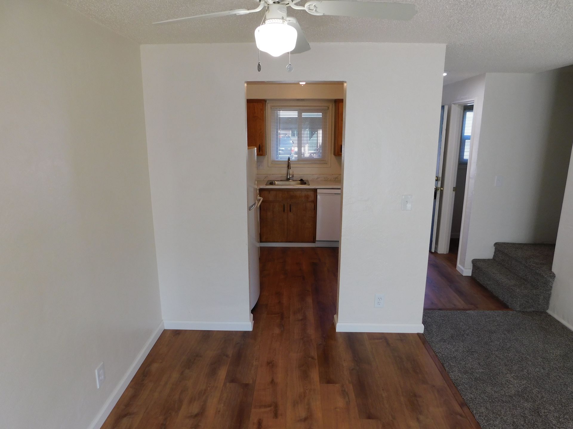 View of a kitchen through an arched doorway.  Dark wood floors, white walls, and a ceiling fan.