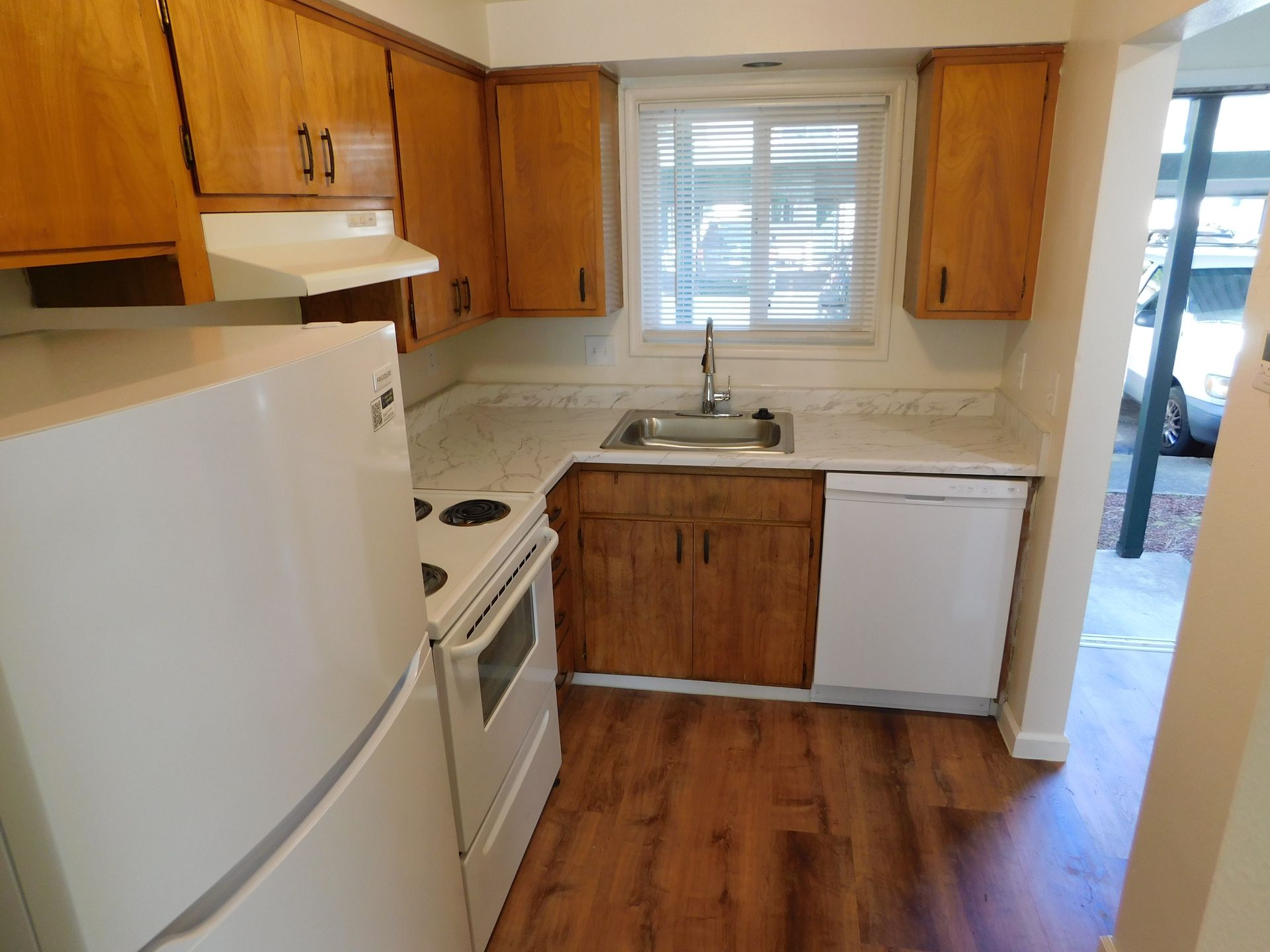 Small kitchen with wooden cabinets, white appliances, and a window.