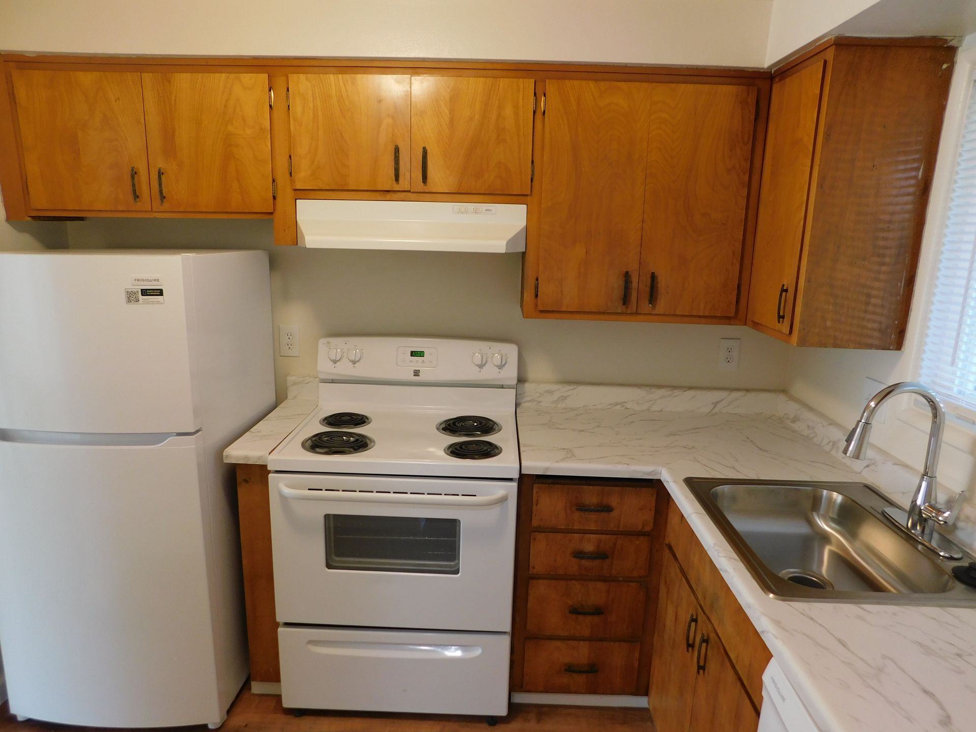 Kitchen with white appliances, light wood cabinets, and a stainless steel sink.