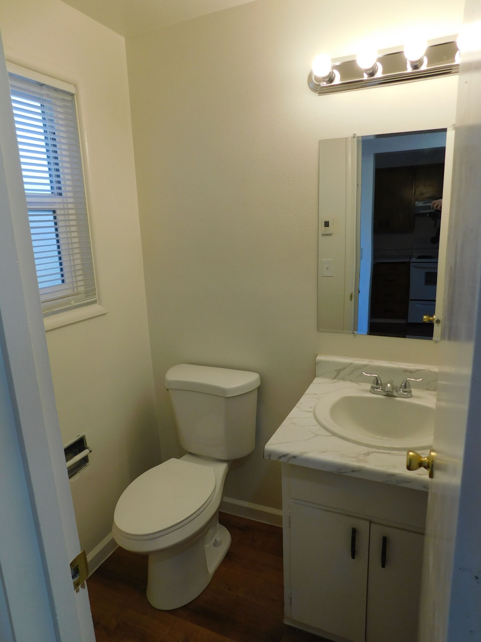 Small bathroom with toilet, vanity, mirror, and window; white and beige color scheme.
