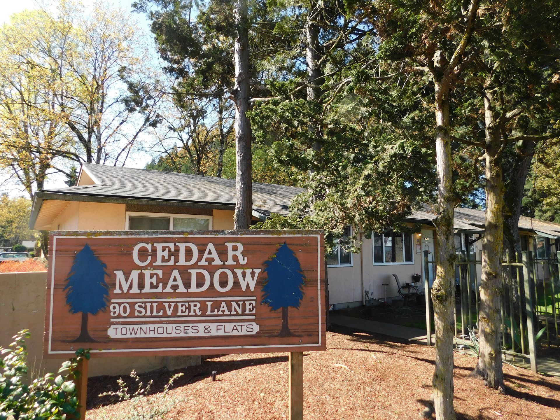 Cedar Meadow sign, brown with blue trees, in front of tan building, 90 Silver Lane.