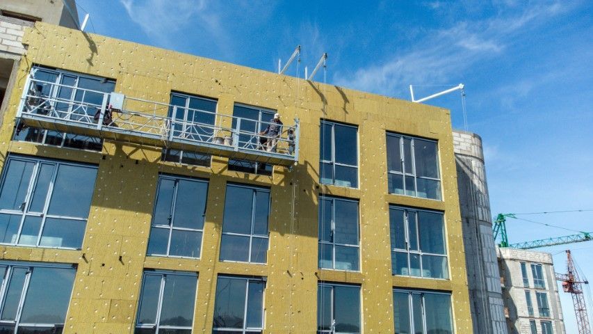 Building exterior under construction with scaffolding and windows. The building is covered in yellow insulation.