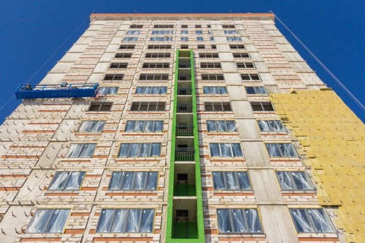 High-rise building under construction with scaffolding and a work platform against a blue sky.
