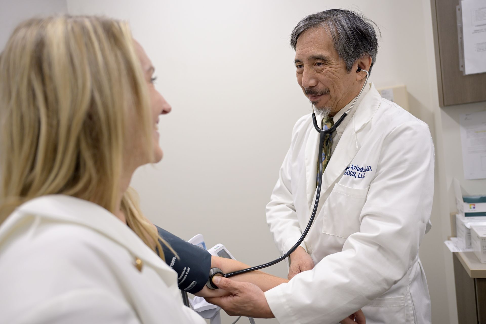 Doctor in lab coat with stethoscope taking patient blood pressure.