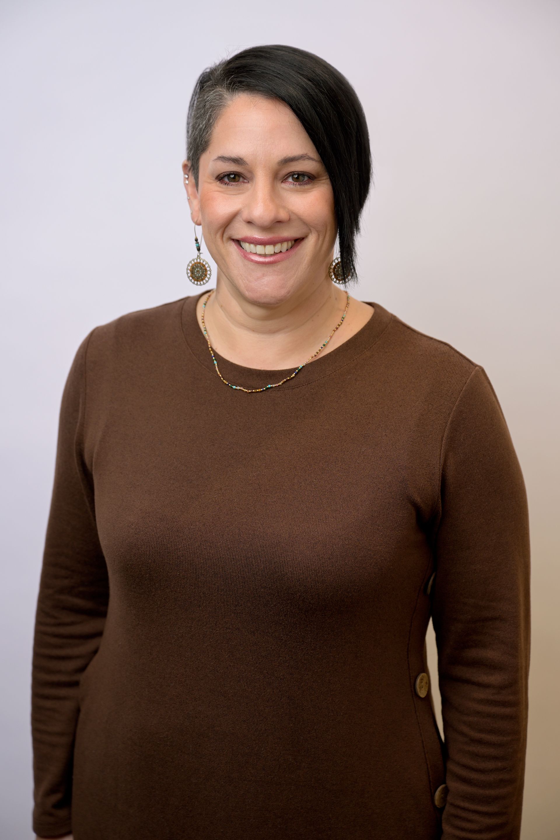 Woman wearing glasses and a stethoscope, smiling, in a white lab coat.