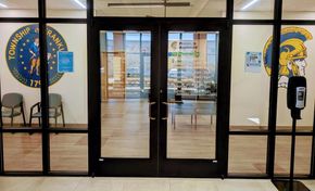 Glass doors of Franklin Township building, framed by black. Logos on walls, chairs to the left, hand sanitizer to the right.