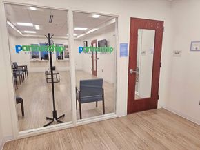 Entrance to a medical office with glass windows, a coat rack, and chairs in a waiting area.