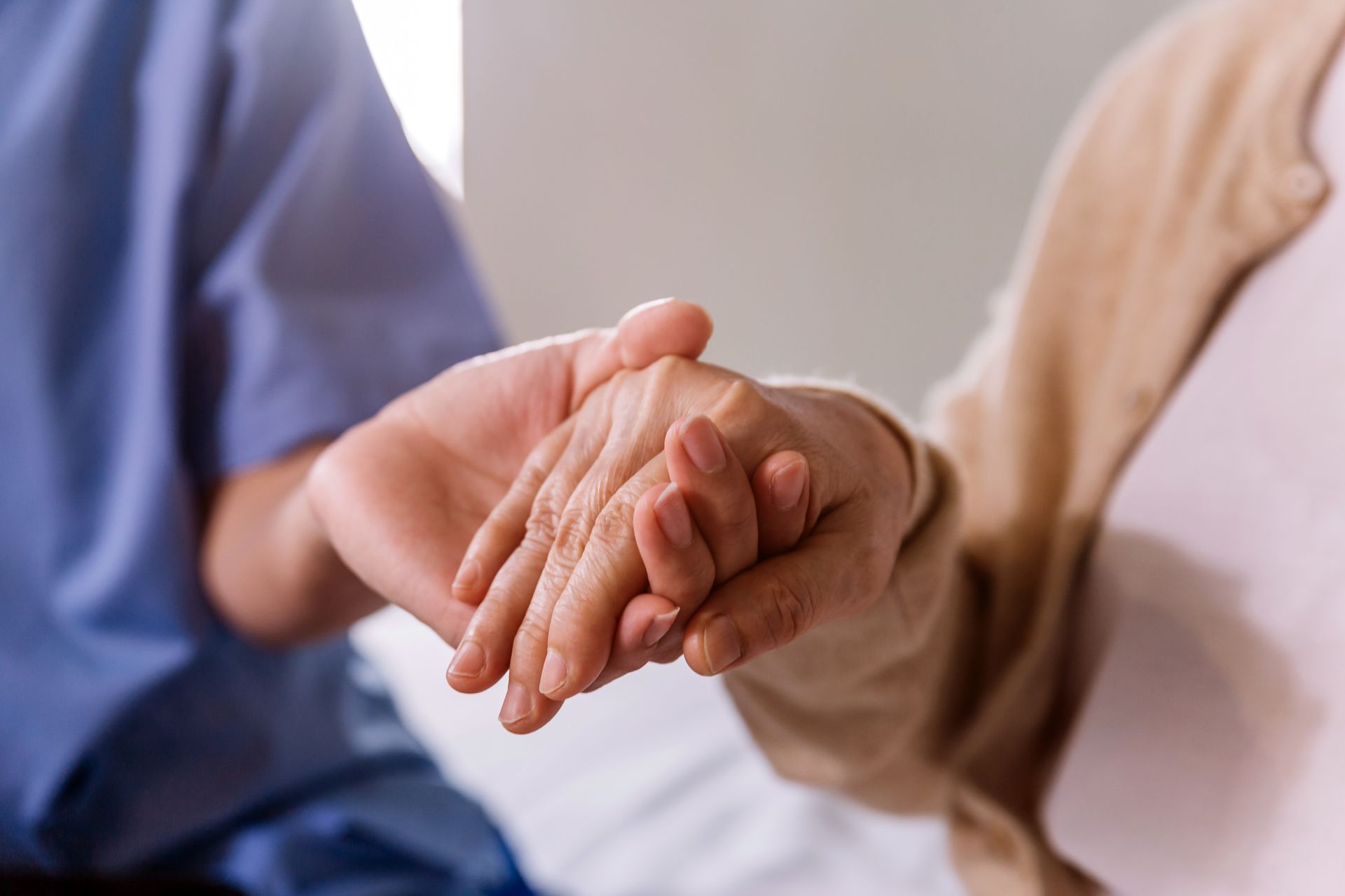 Person in blue uniform gently holds the hand of someone in a beige sweater, indoors.