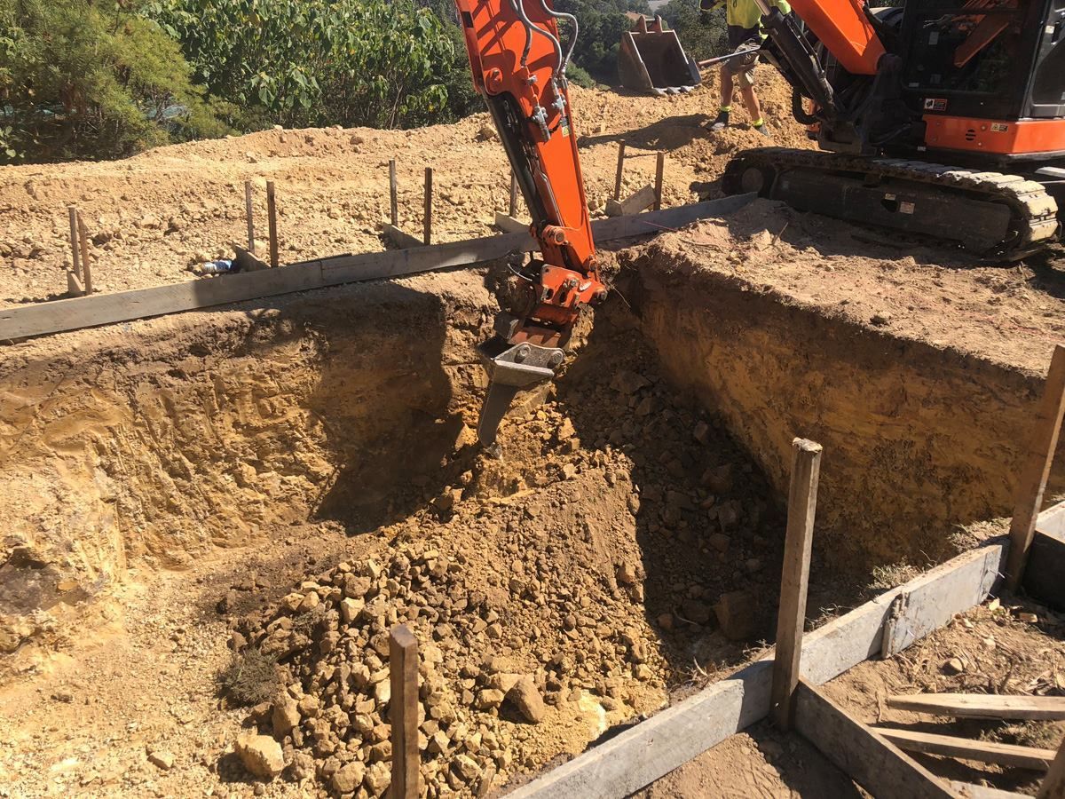 Excavator digging in a construction site, brown soil, wooden stakes, and concrete forms. — Banora Pools in Tweed Heads South, NSW
