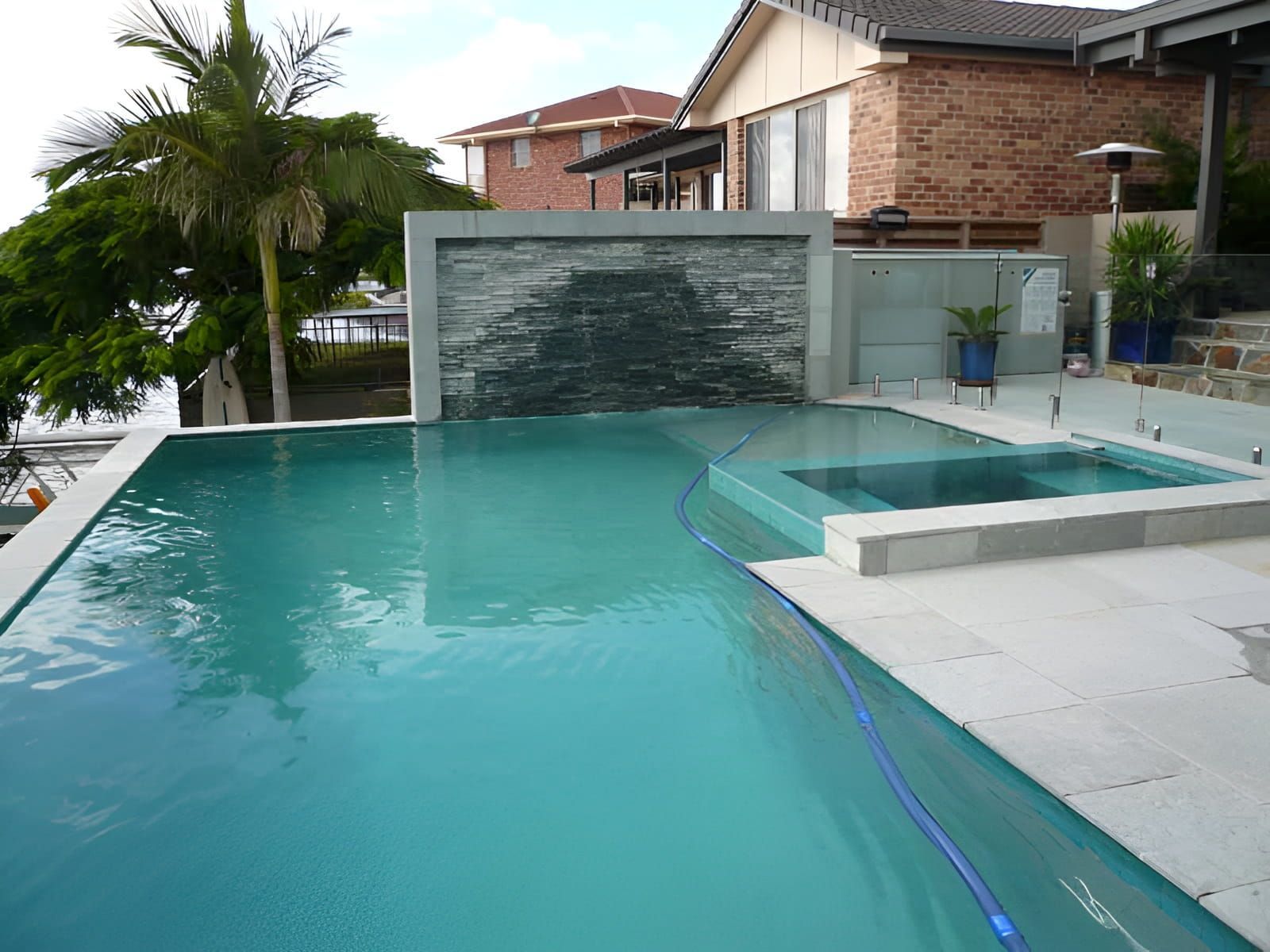 Swimming pool with waterfall feature, a separate spa, and a view of houses. — Banora Pools in Ballina, NSW
