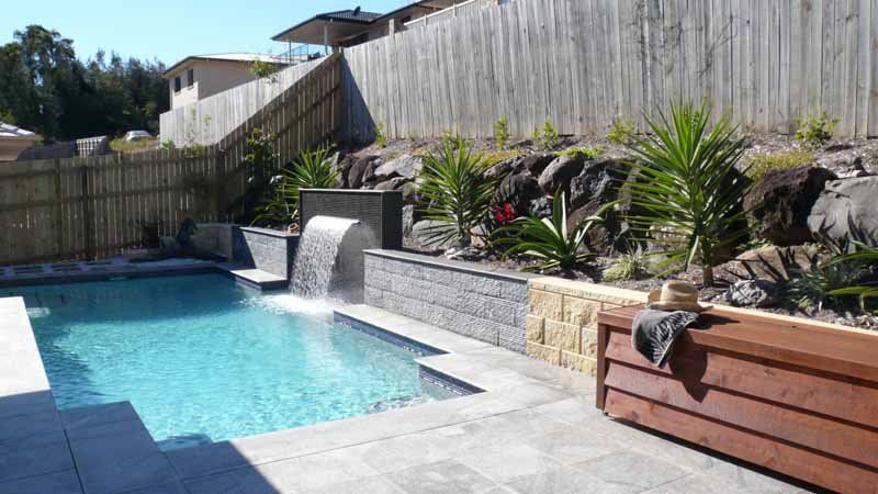 Swimming Pool With Waterfall Feature, Surrounded by Landscaping and a Wooden Bench — Banora Pools in Tweed Heads South, NSW