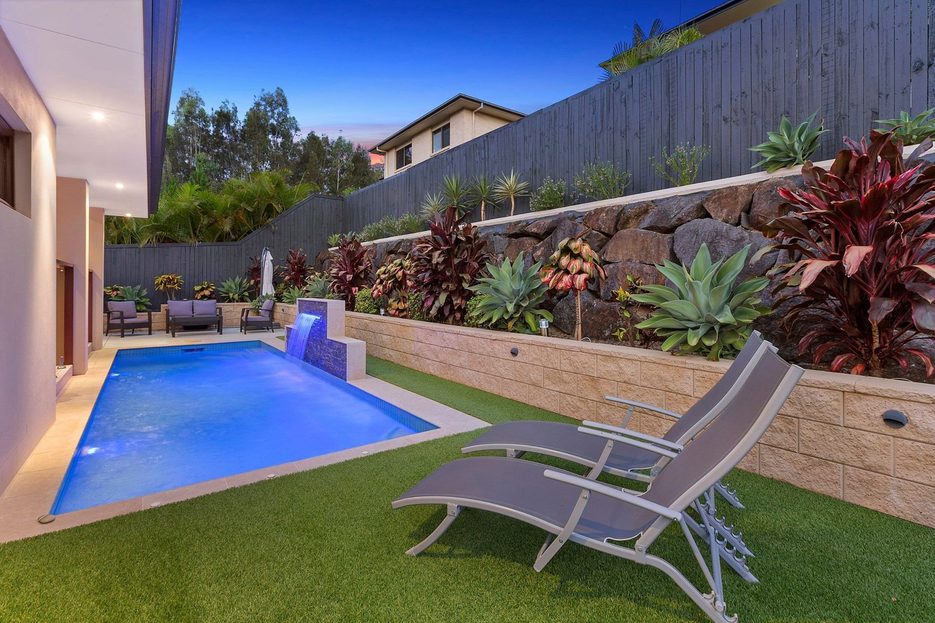 Poolside scene with a blue pool, lounge chairs, and tiered garden with colorful plants. — Banora Pools in Tweed Heads South, NSW