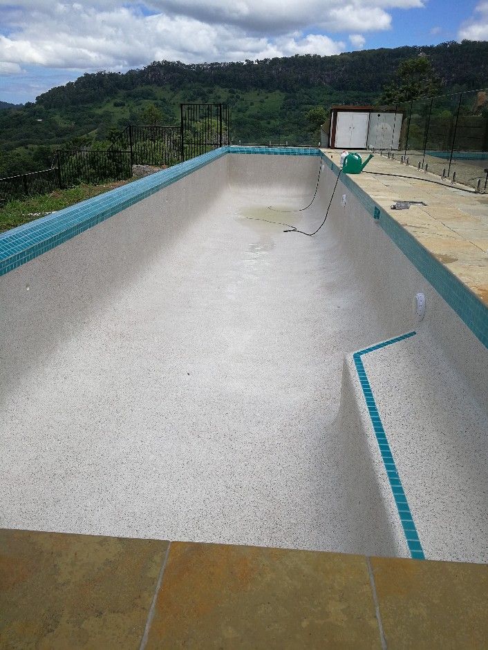 Empty swimming pool, white interior, turquoise tile trim, overlooking green hills under a cloudy sky. — Banora Pools in Tweed Heads South, NSW