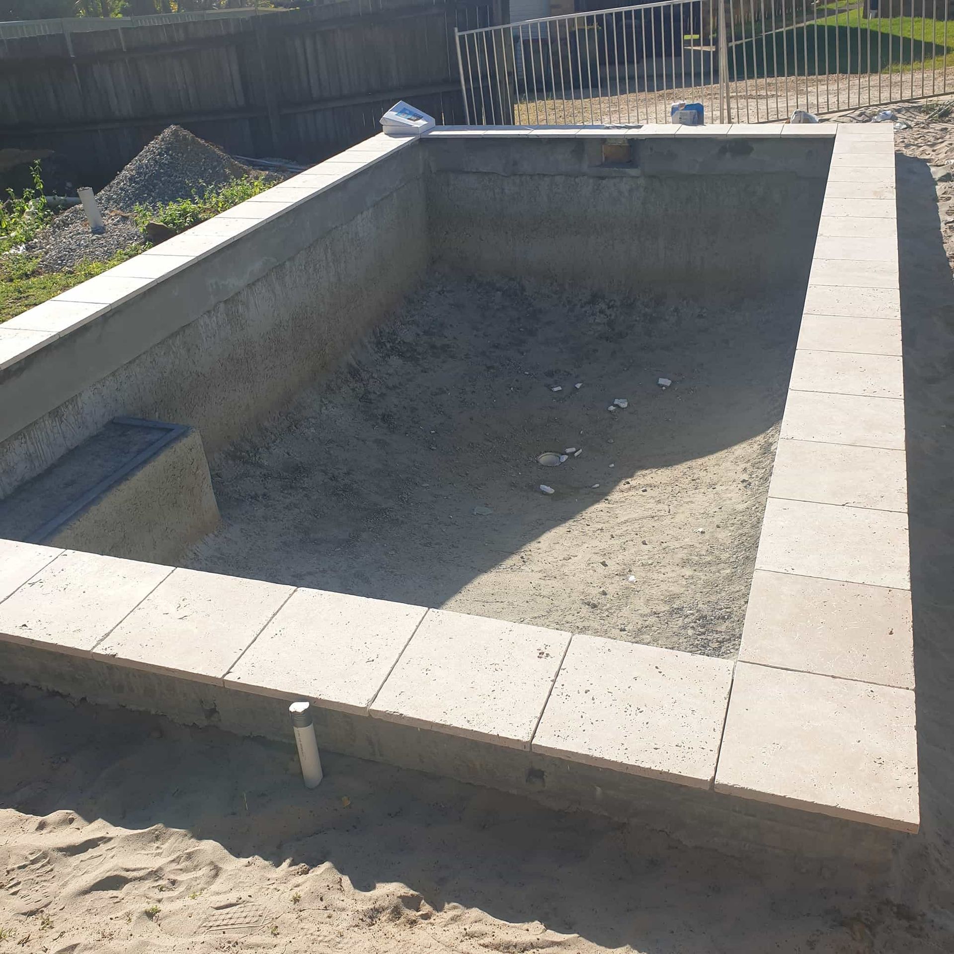 Unfinished rectangular pool with concrete edging, in a dirt yard. A small bench is visible in the pool. — Banora Pools in Tweed Heads South, NSW