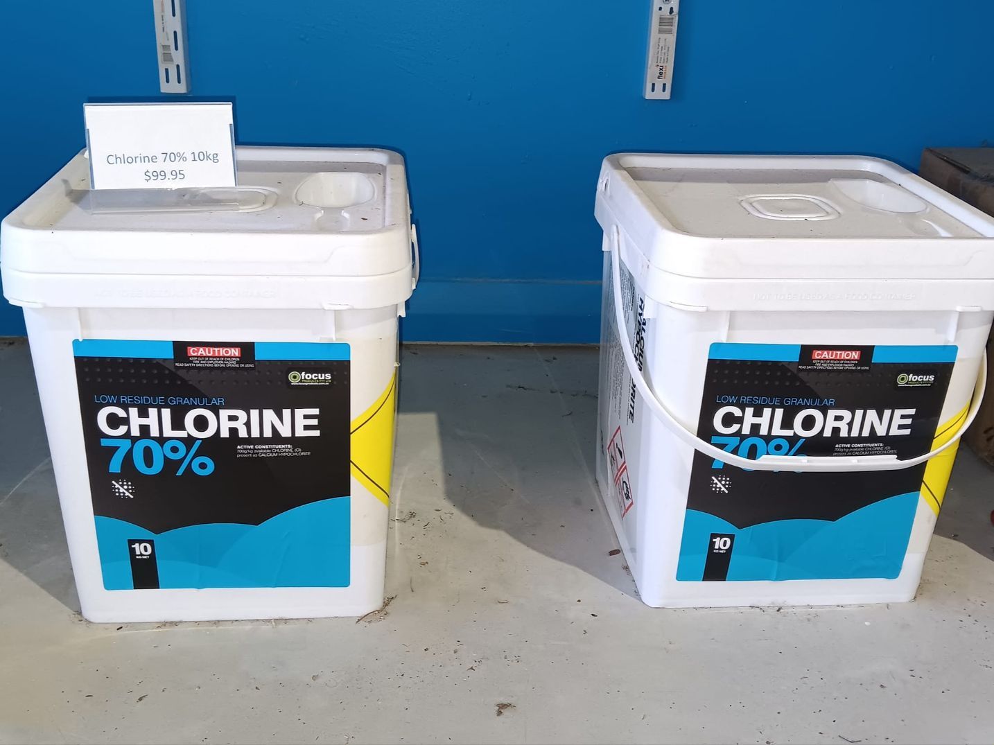 Two White Buckets of 70% Chlorine With Blue and Yellow Labels Against a Blue Wall — Banora Pools in Tweed Heads South, NSW