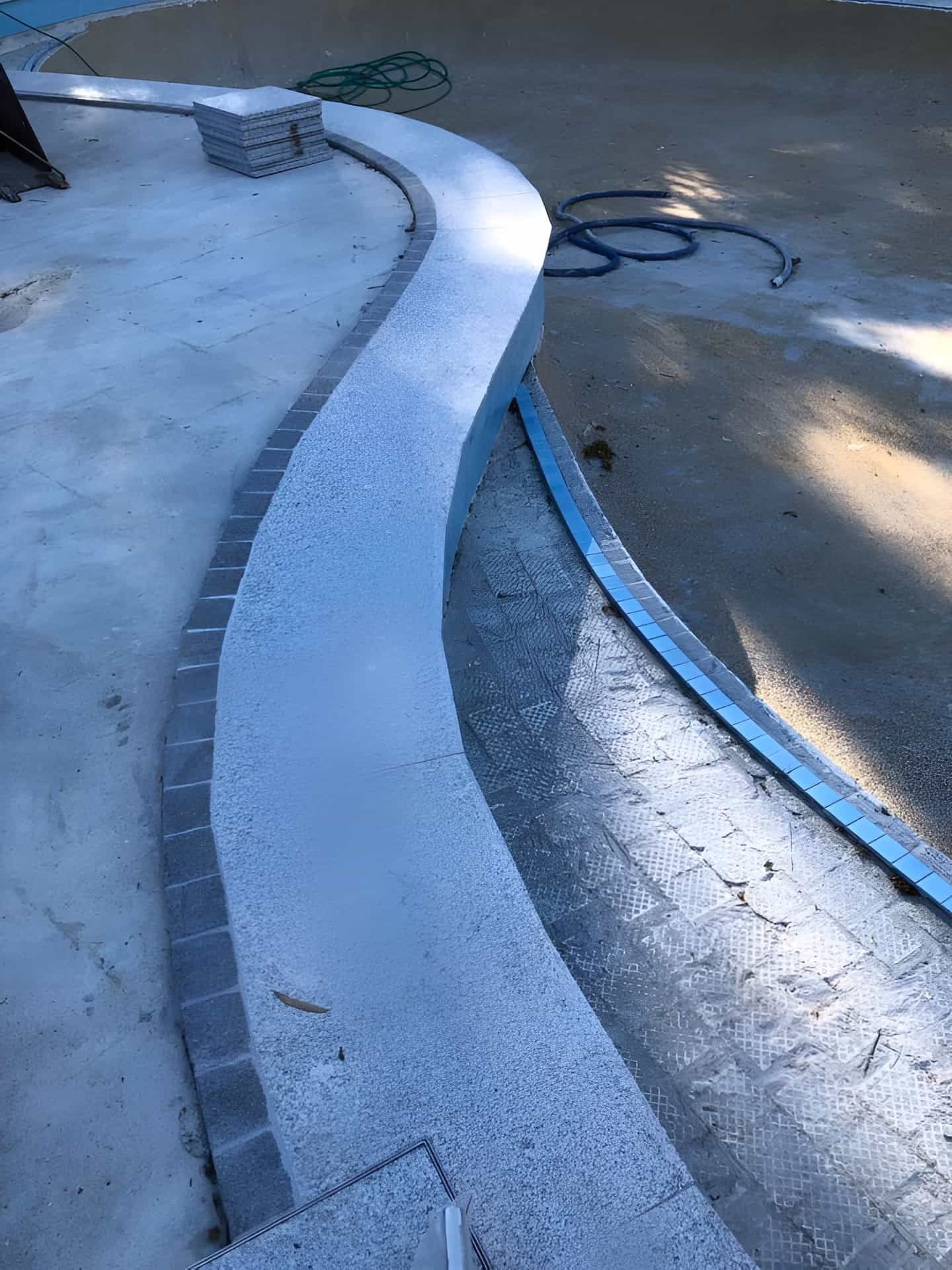 Curved concrete pathway with stacked grey bricks and metal edging, next to a pool under construction. — Banora Pools in Mullumbimby, NSW