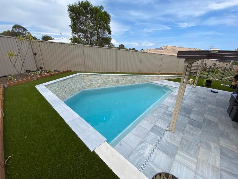 A pool with blue water, surrounded by white tile and green turf, in a backyard with a fence. — Banora Pools in Pottsville, NSW