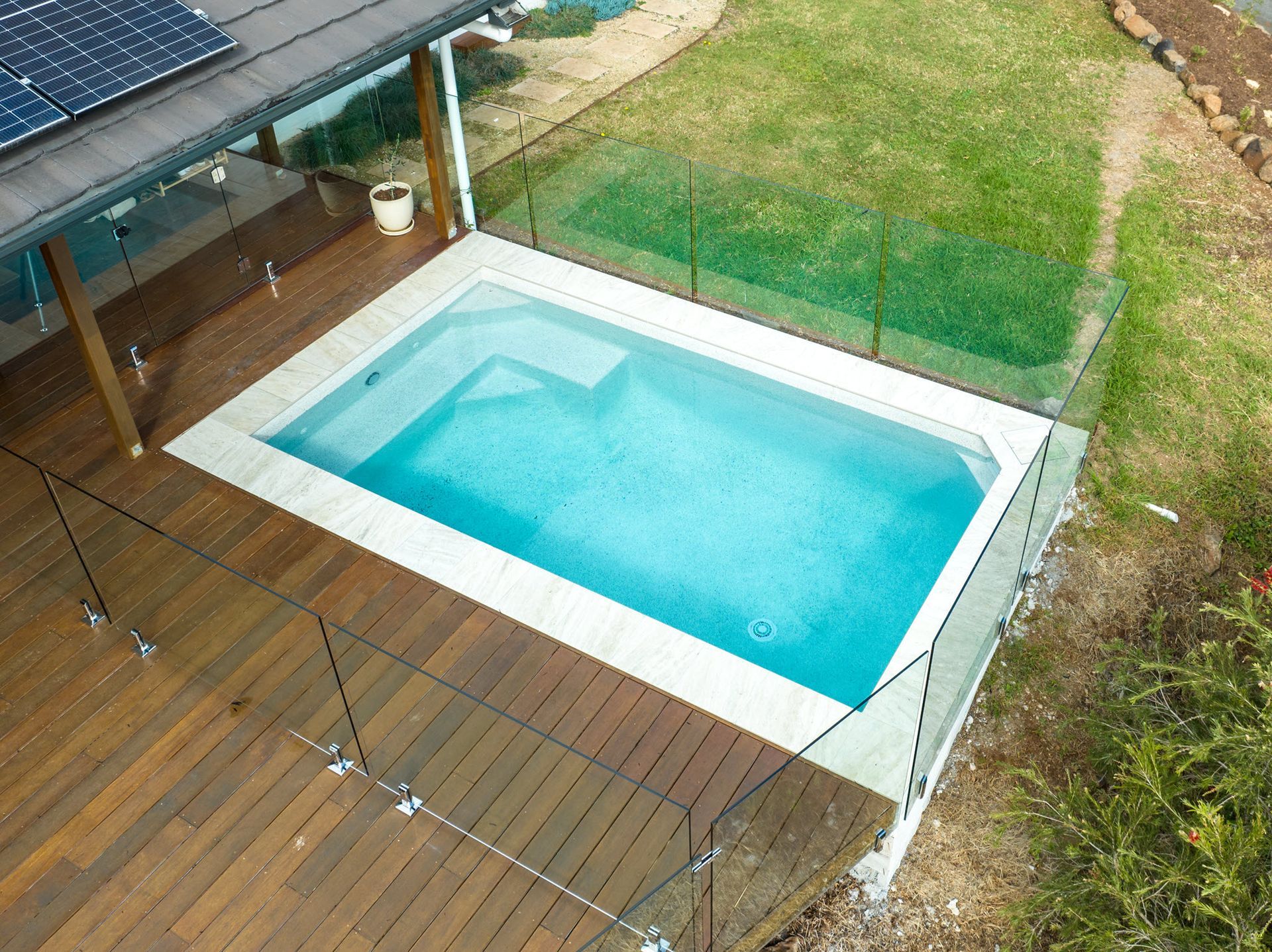Small rectangular pool surrounded by decking and grass, enclosed by a black fence.