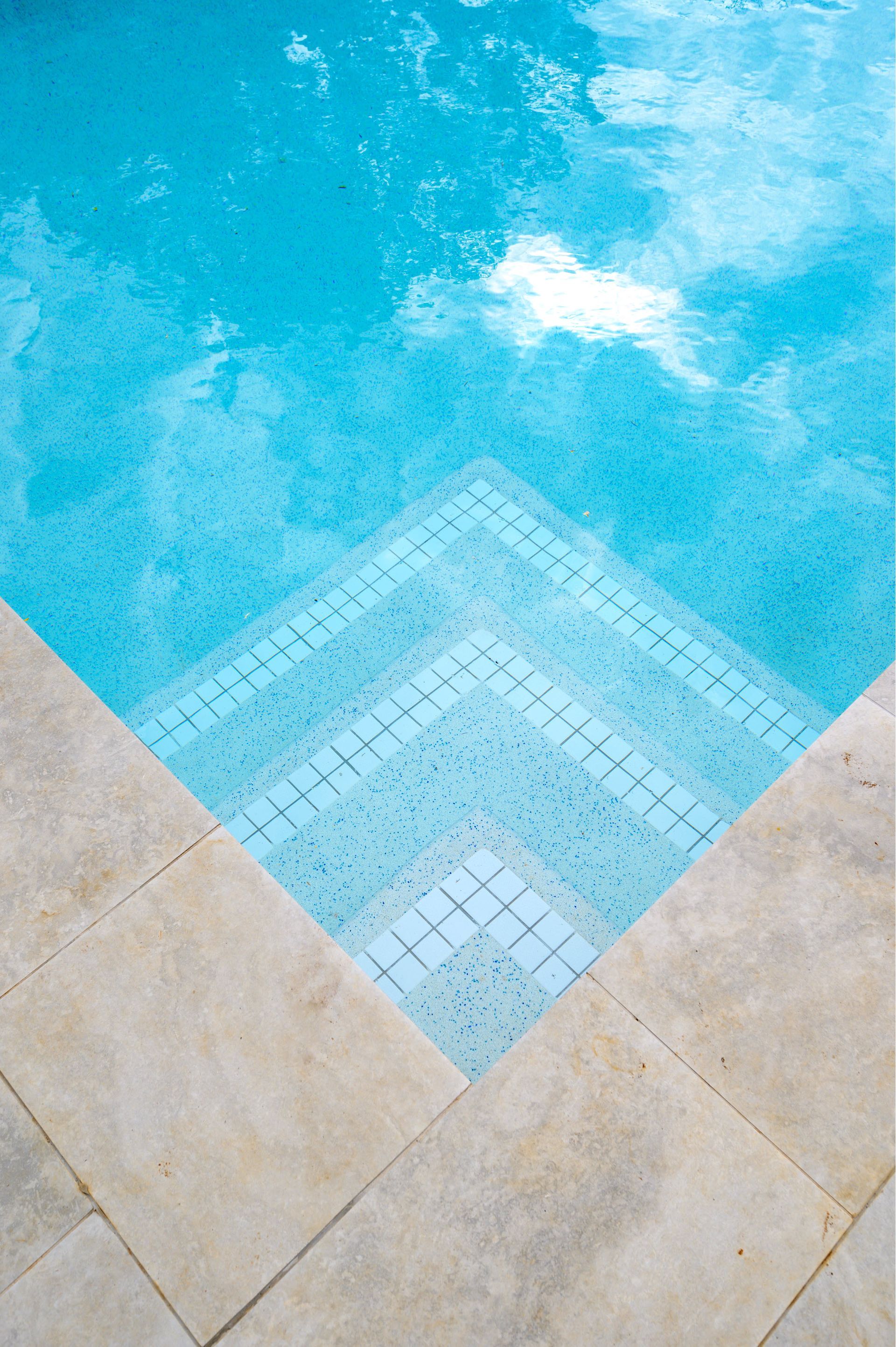 Pool steps descend into turquoise water, bordered by beige stone.