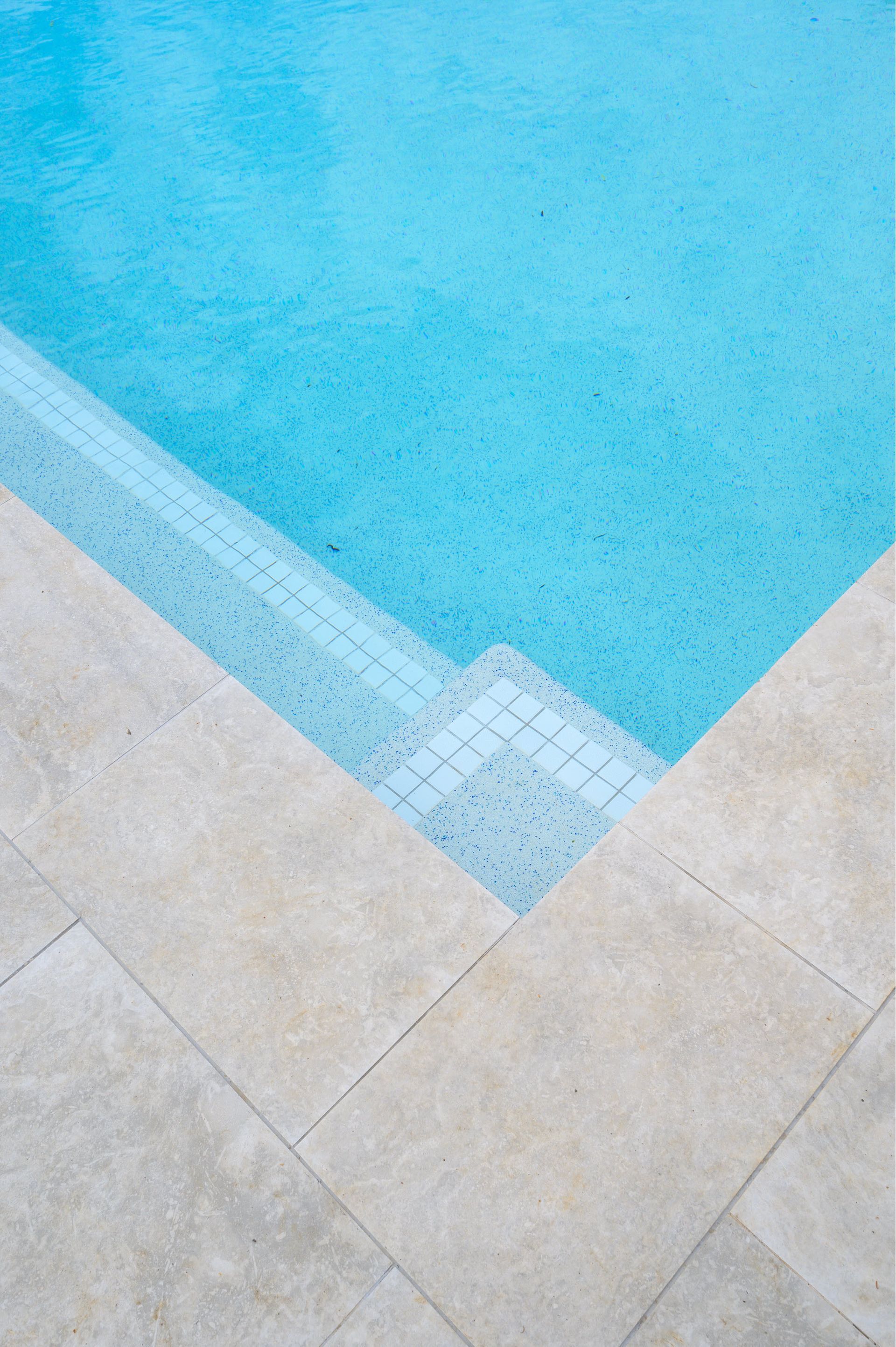 Light blue pool with white tile steps, beige stone border.