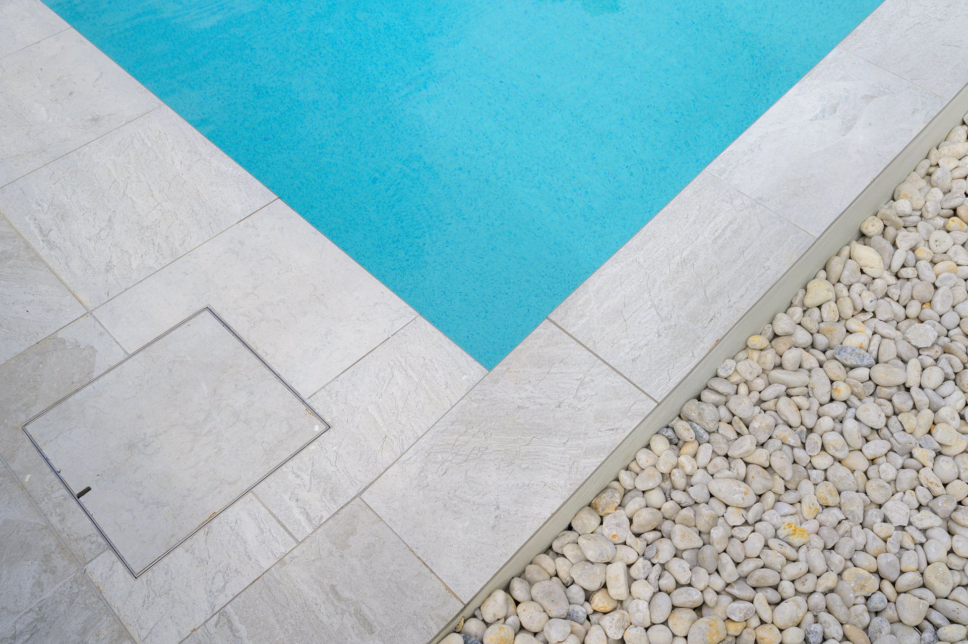 Pool edge with light blue water, stone tiles, and white pebbles.