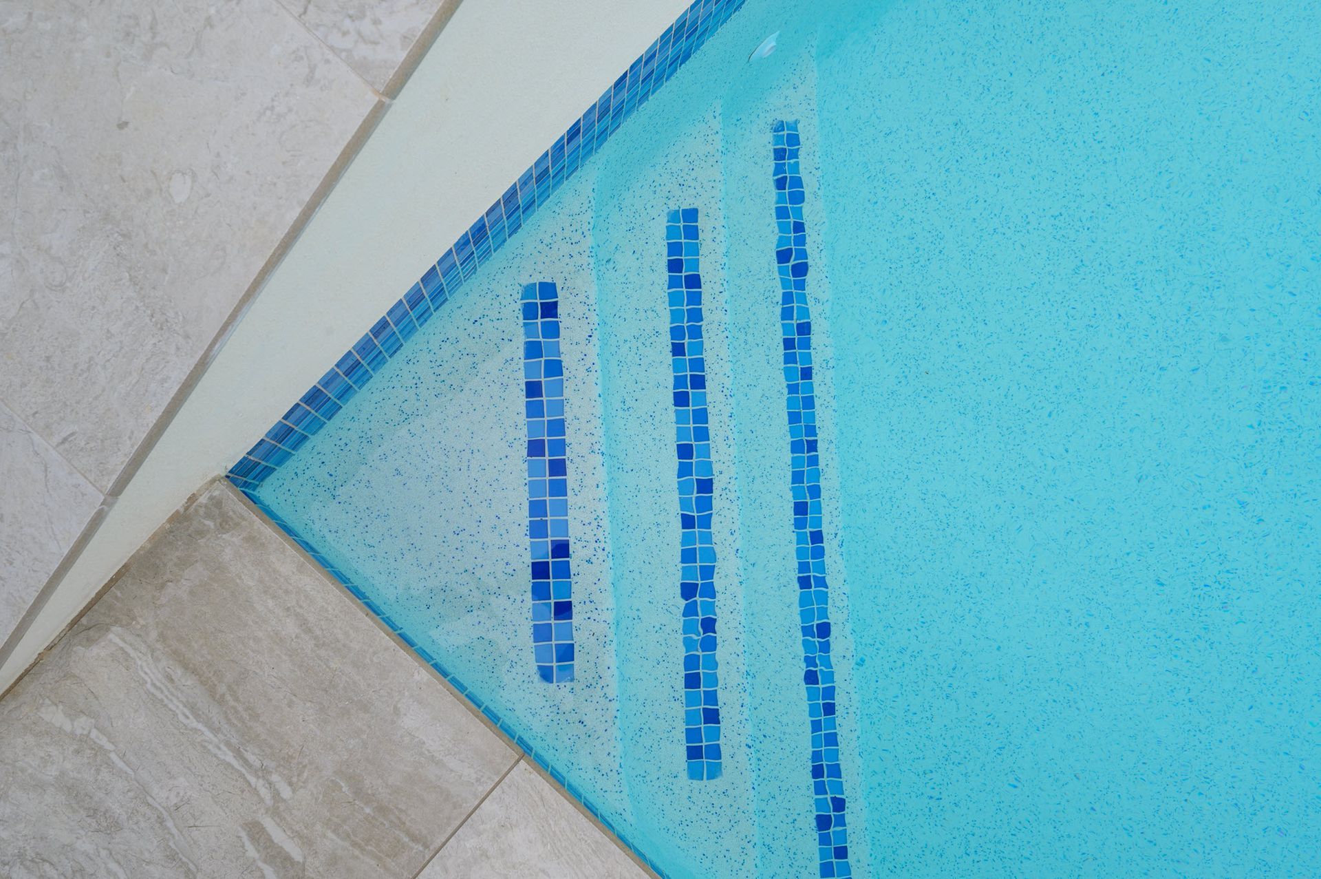 Pool steps with blue tile detail, turquoise water, light gray tiles surrounding.