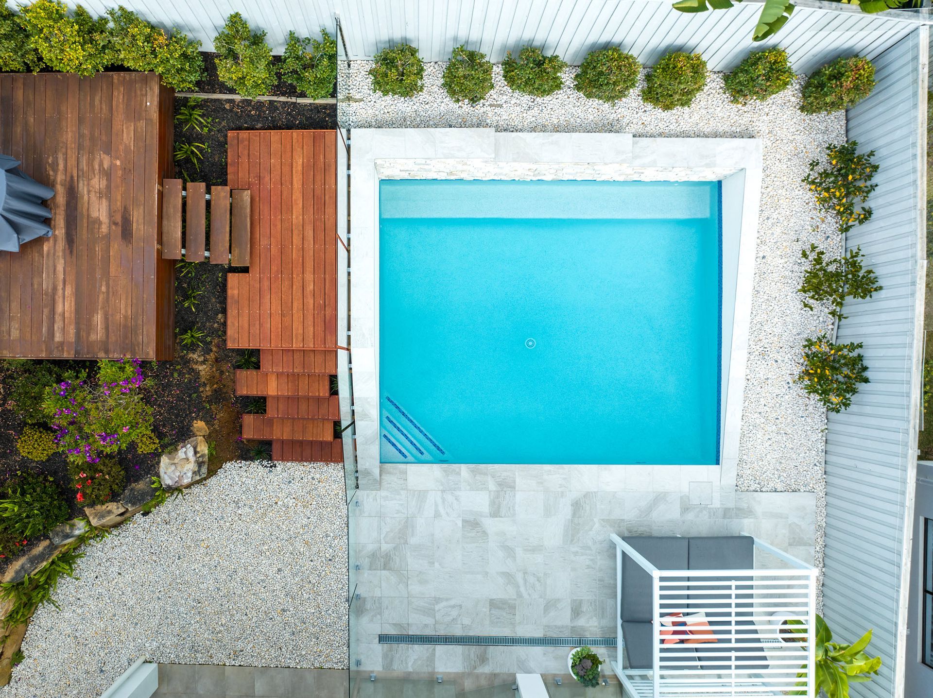 Aerial view of a backyard with a pool, deck, and landscaping in a modern design.