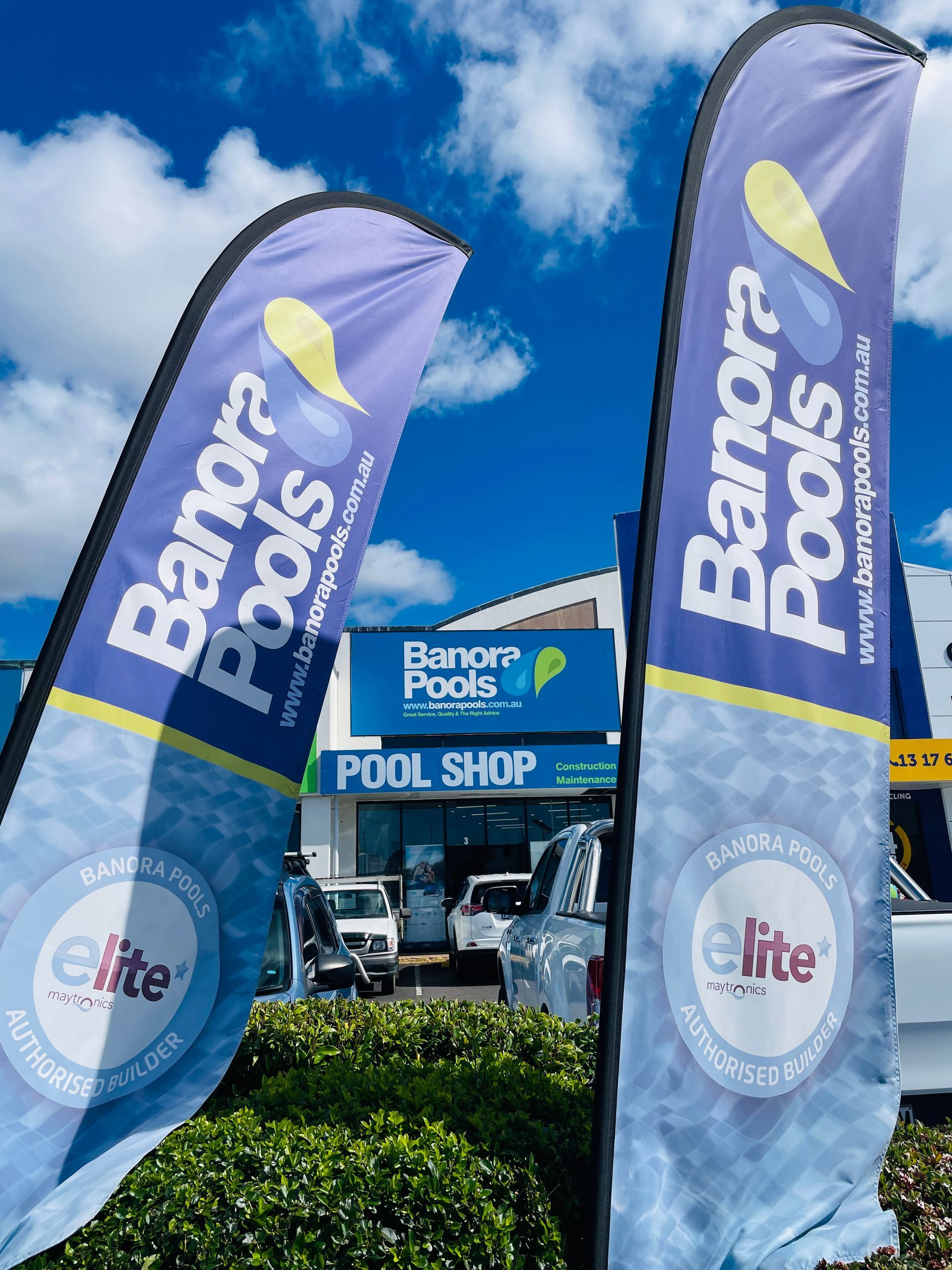 Two blue and yellow Banora Pools flags outside a pool shop with a blue sky. — Banora Pools in Tweed Heads South, NSW