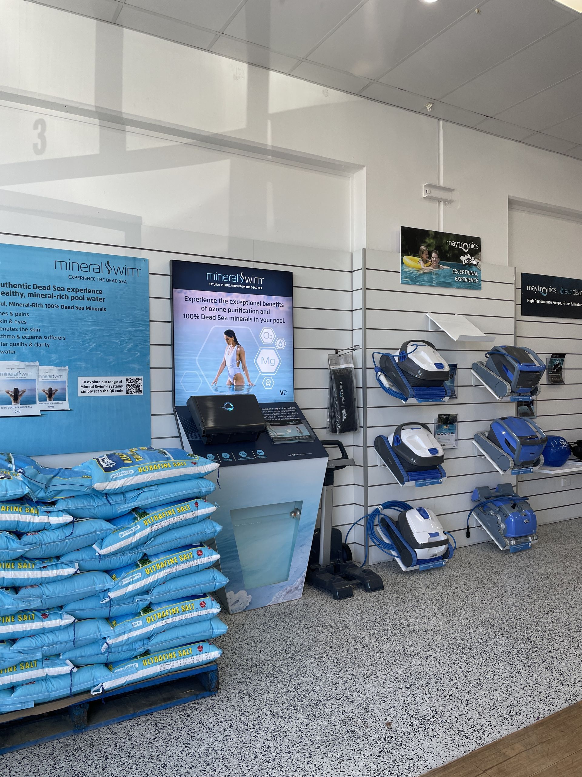 Pool supplies store display: bags of chemicals, robotic pool cleaners, and promotional signage. — Banora Pools in Tweed Heads South, NSW