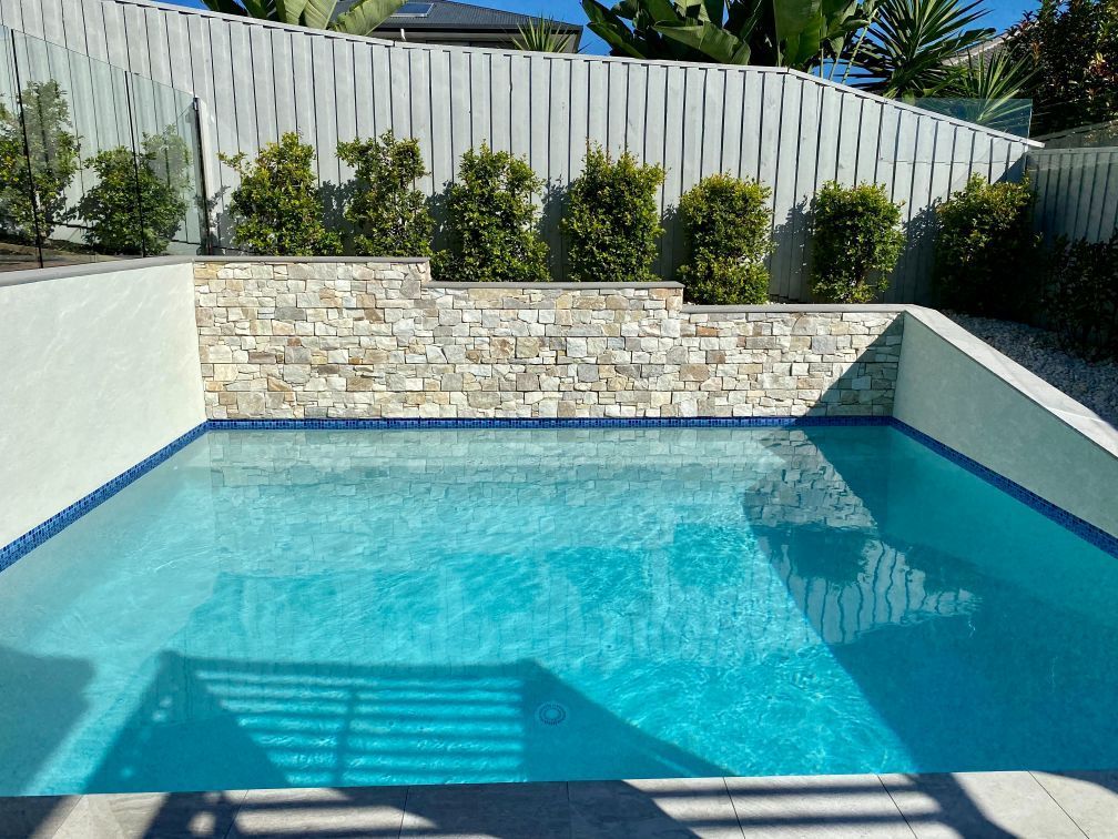 Pool With Turquoise Water and Stone Wall, Surrounded by Landscaping and a White Fence — Banora Pools in Tweed Heads South, NSW