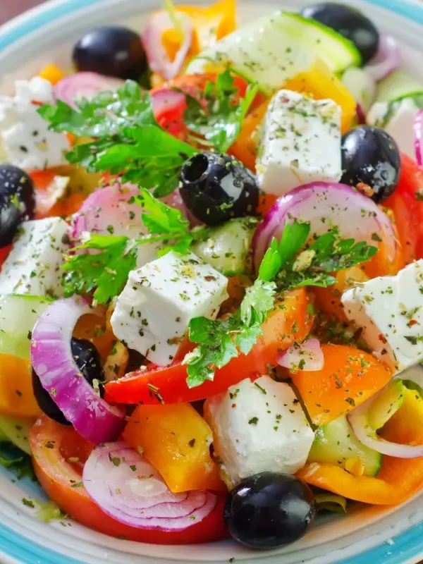 A salad with tomatoes , cucumbers , onions , olives and feta cheese on a plate.